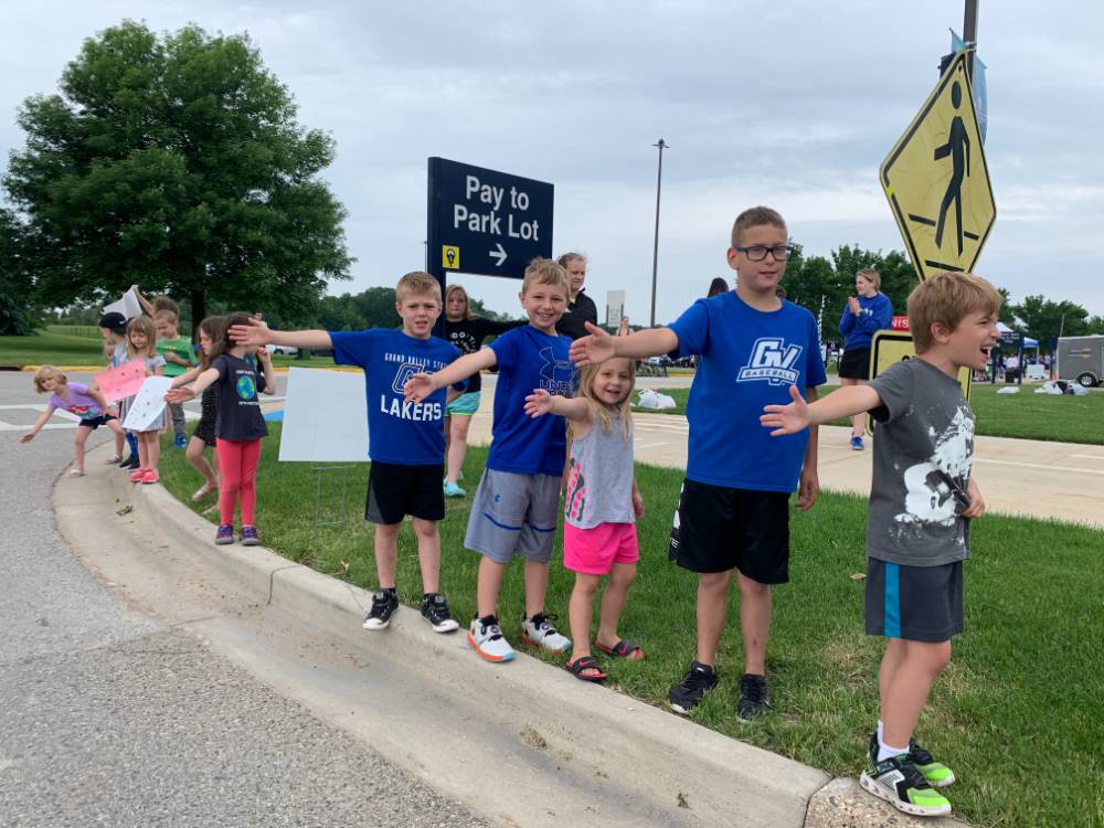 Children from the GVSU Children's Enrichment Center standing on a street curb and holding out their hands to receive high-fives from the racers